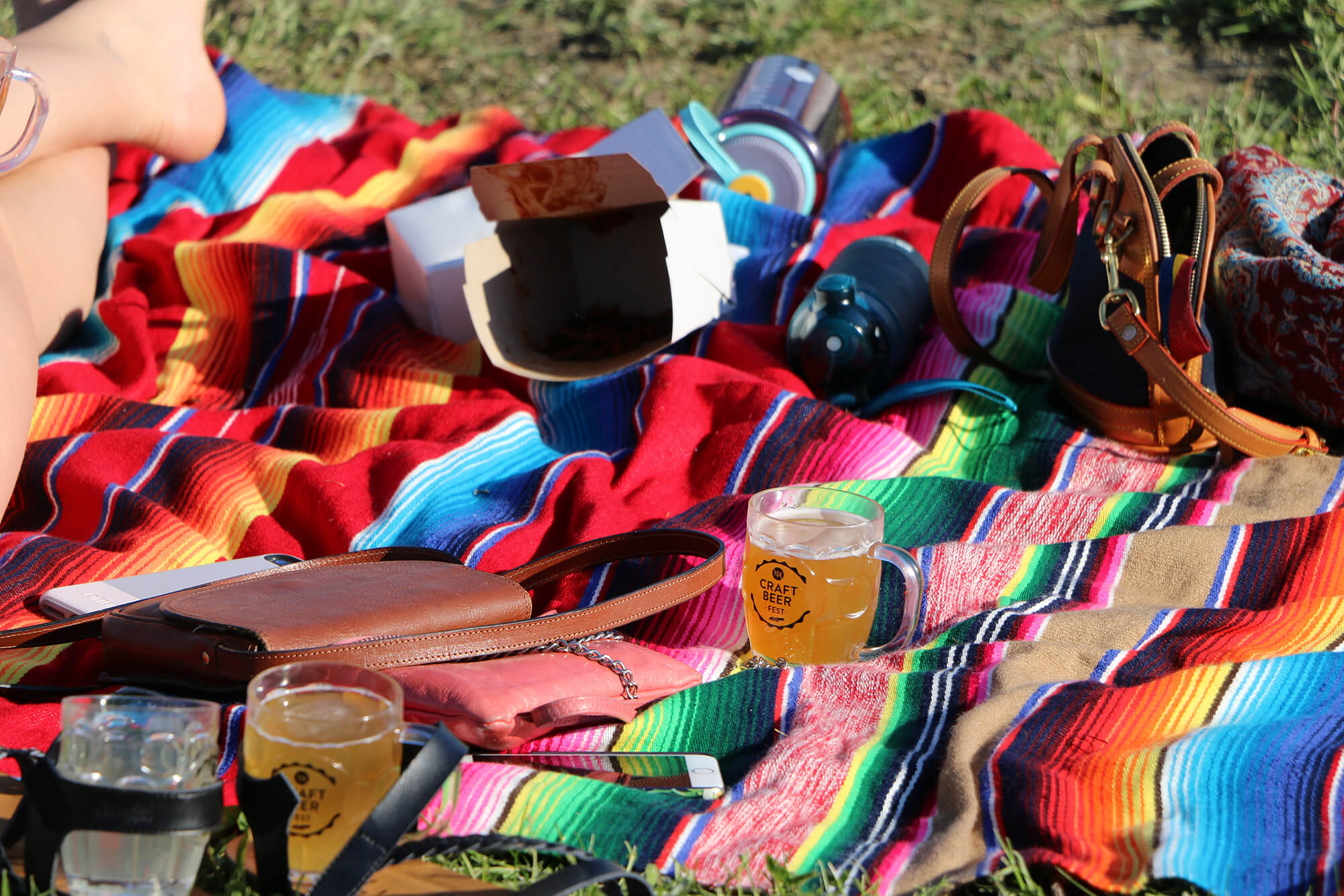 Colourful blanket on grass with mug filled beer with purse and personal belongings