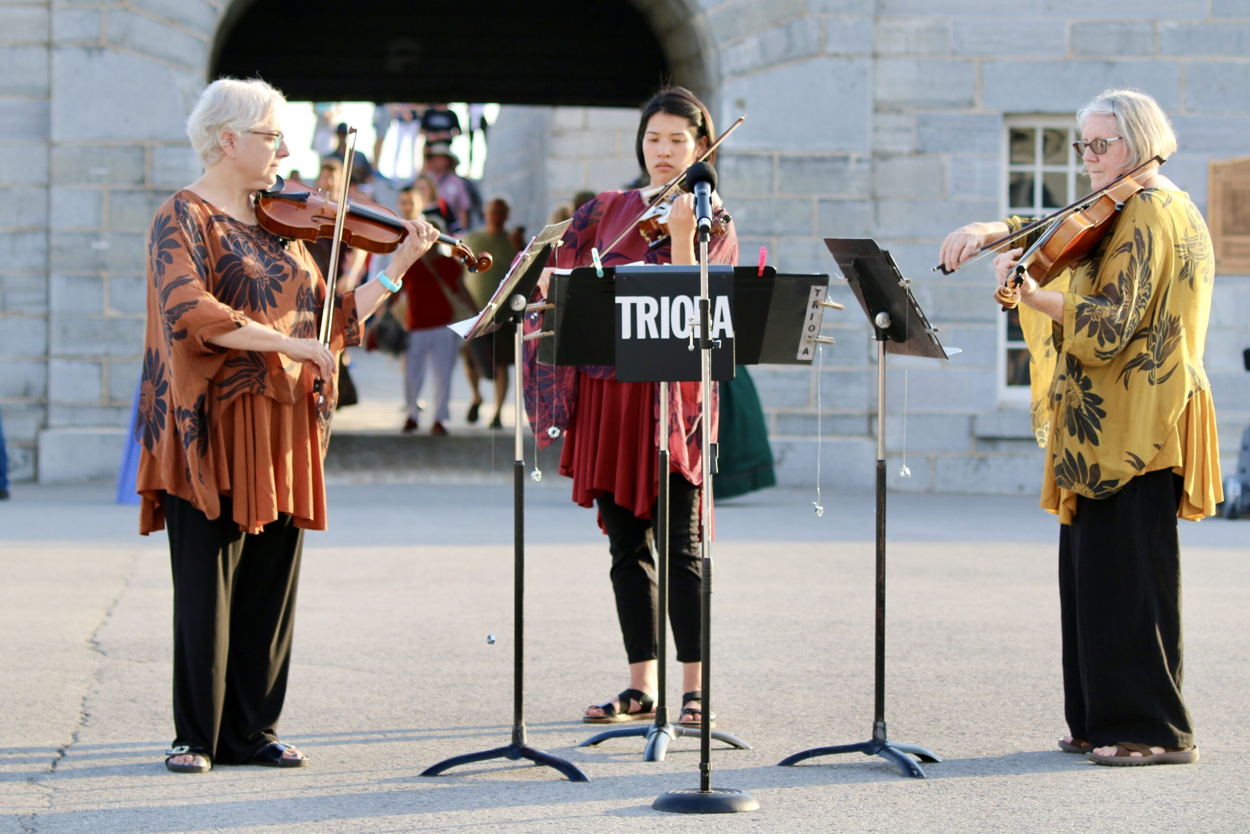 Three female playing violin on parade square at Fort Henry.